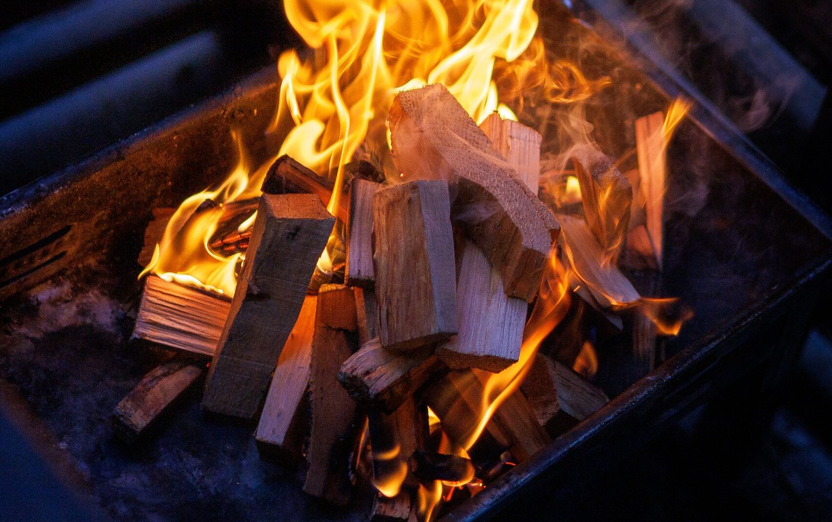 A vivid campfire burning brightly in a dark grill, offering a warm, inviting glow.