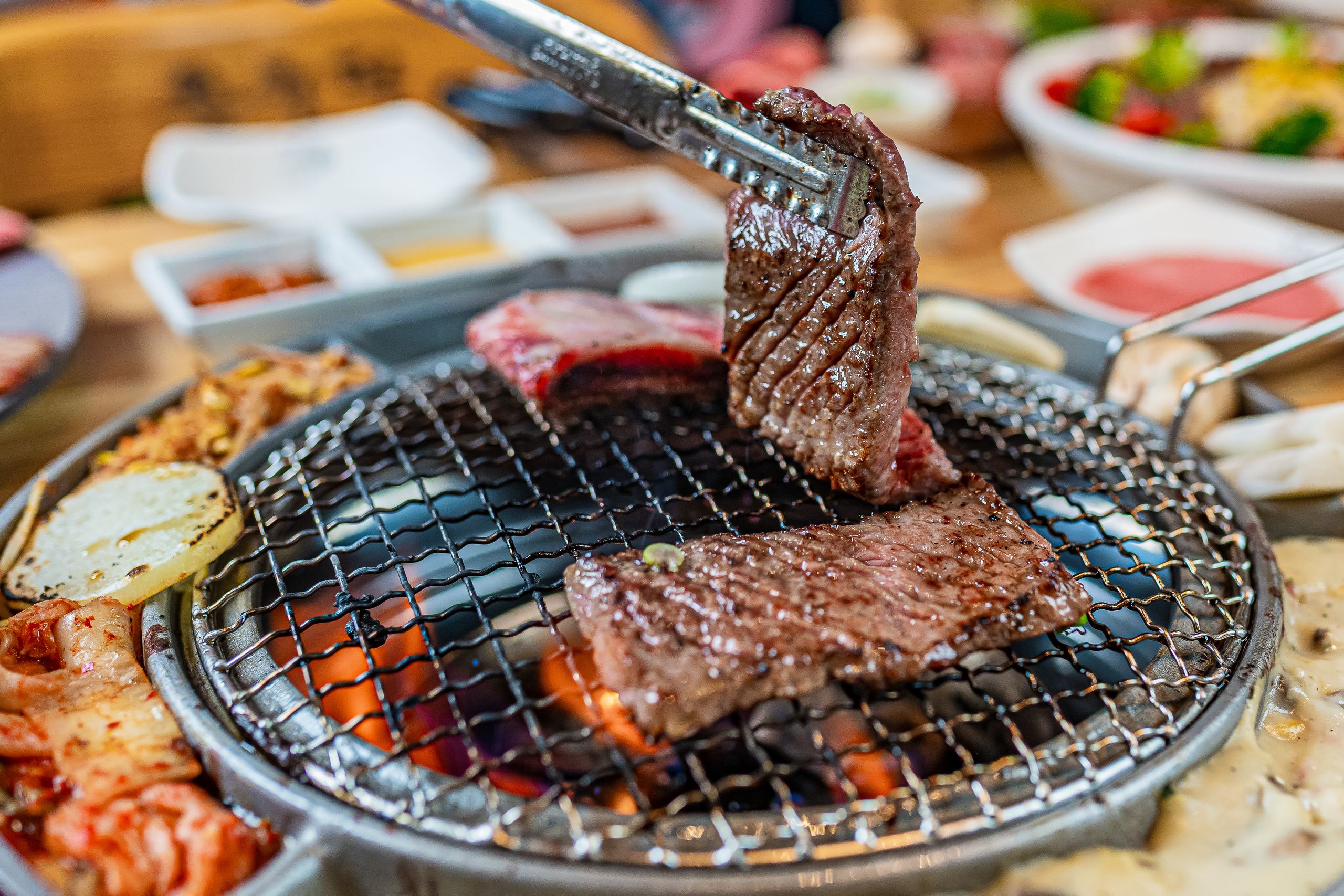 Juicy cuts of meat being grilled on a barbecue with tongs for a delicious meal.