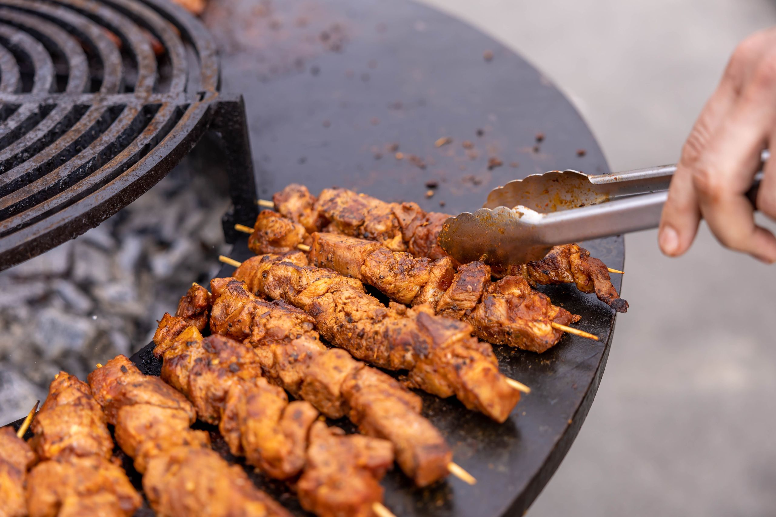 Close-up of meat skewers grilling outdoors, highlighting texture and flavor.