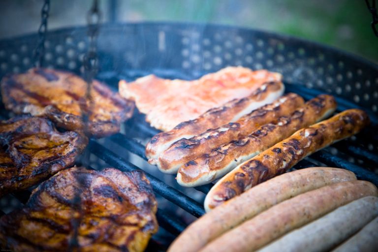 Close-up of various meats including sausages grilling outdoors on a barbecue.