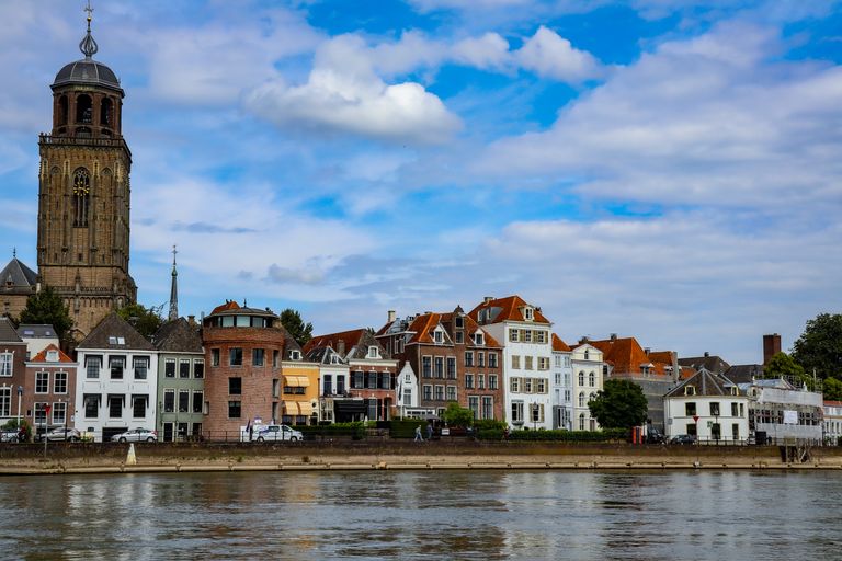 Picturesque cityscape of Deventer with iconic church tower and riverside houses under blue sky.